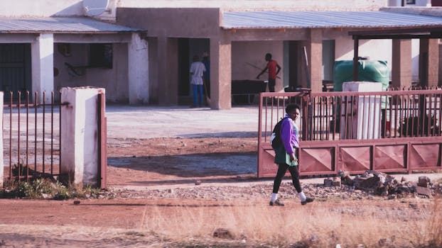 A child in uniform walks past a rural South African home on a sunny day.