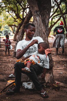 A heartwarming moment of a father and child resting under the trees in a Luanda park.