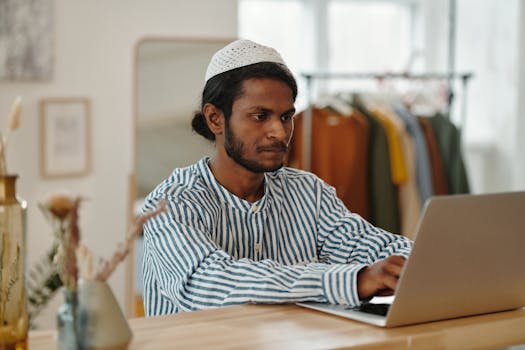 A man in stripes works intently on a laptop indoors, showcasing productivity and focus.
