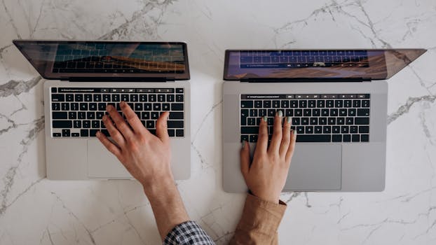 Top view of hands typing on two laptops, showcasing collaboration and technology.